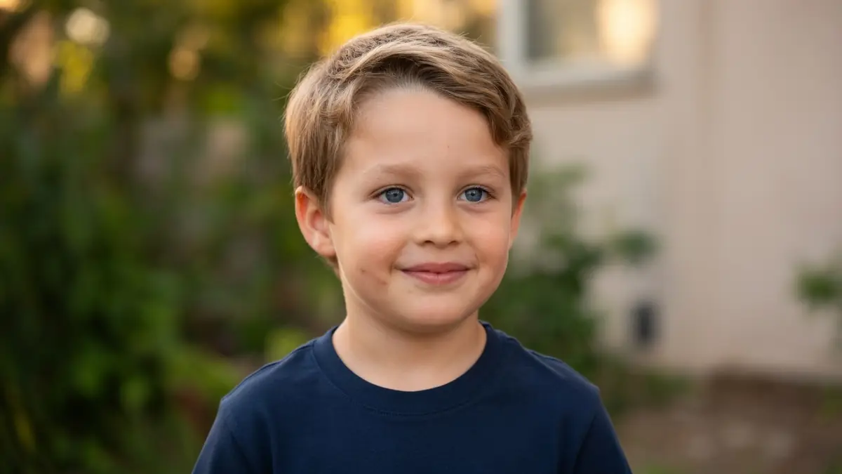 Portrait d'un jeune garçon aux yeux bleus nommé Corentin Guillot souriant devant un jardin flou