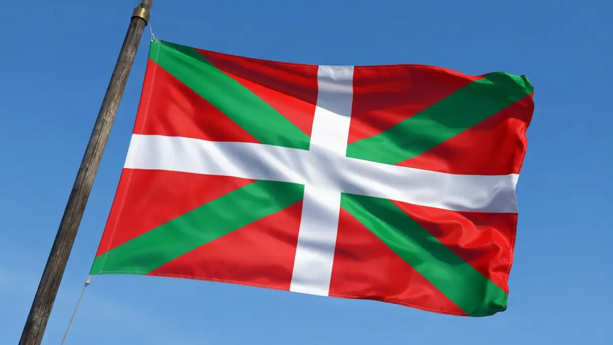 Un drapeau Basque ondule au vent sur un mât en bois devant un ciel bleu