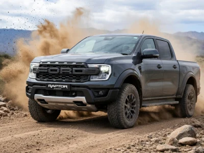 Un Ford Raptor gris soulève de la poussière en roulant sur un chemin de terre rocailleux