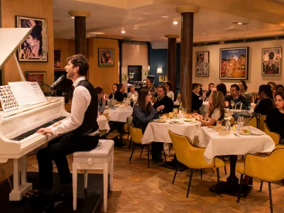 Un pianiste en gilet joue dans le P'tit Piano devant des convives attablés