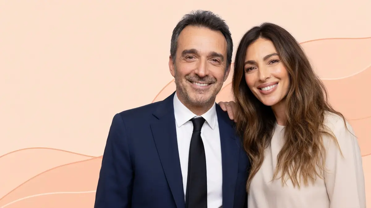 Clément Miserez pose souriant aux côtés d'une femme sur un fond beige aux lignes ondulées