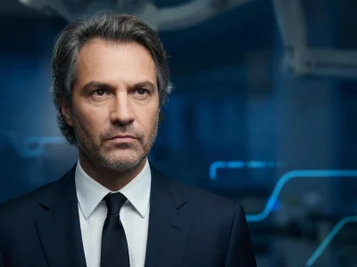 Stéphane Delajou apparaît en costume sombre et cravate sur un fond bleu technologique abstrait