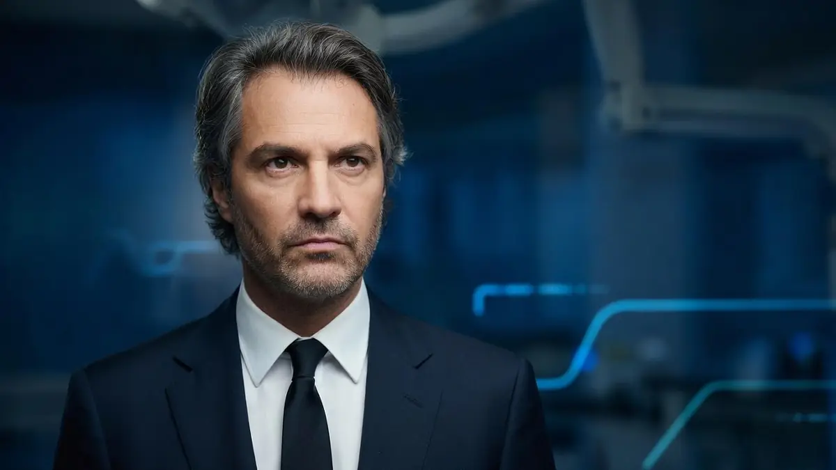 Stéphane Delajou apparaît en costume sombre et cravate sur un fond bleu technologique abstrait