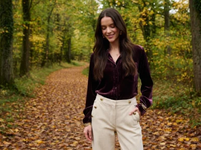 Une femme souriante en pantalon en velours femme sur un sentier automnal
