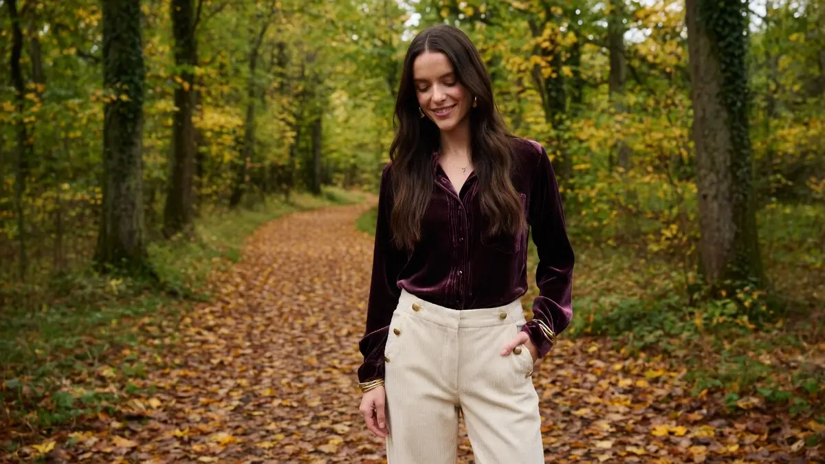 Une femme souriante en pantalon en velours femme sur un sentier automnal