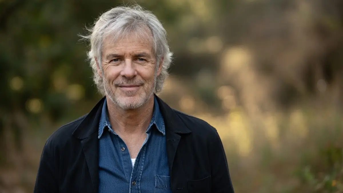 Olivier Pagès sourit légèrement en veste noire devant un fond de verdure flou
