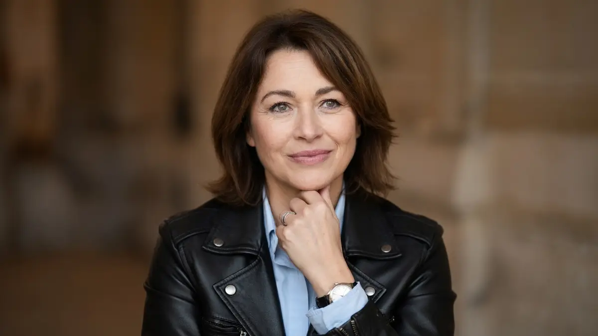 Virginie Caren pose avec sa main sur le menton dans un blouson en cuir noir