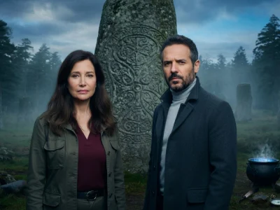 Un homme et une femme enquêteurs posent devant un menhir gravé dans la brume pour les secrets du Finistère