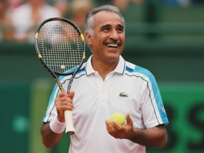 Mansour Bahrami sourit en tenant une raquette et une balle sur un court de tennis