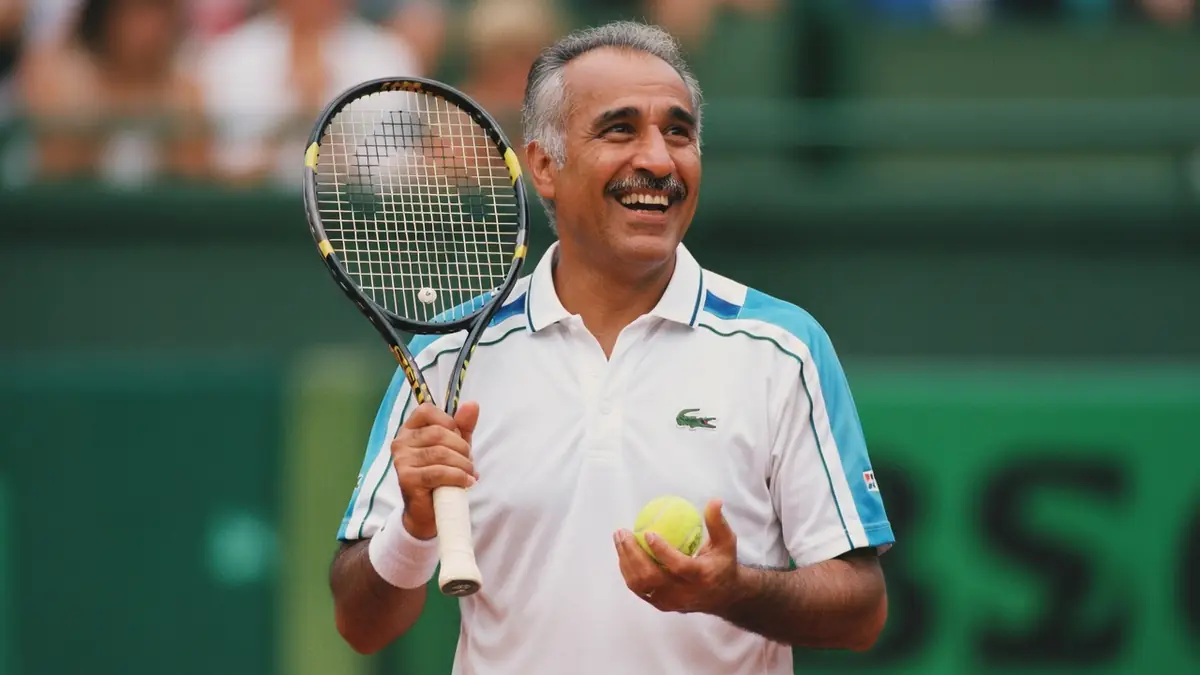 Mansour Bahrami sourit en tenant une raquette et une balle sur un court de tennis