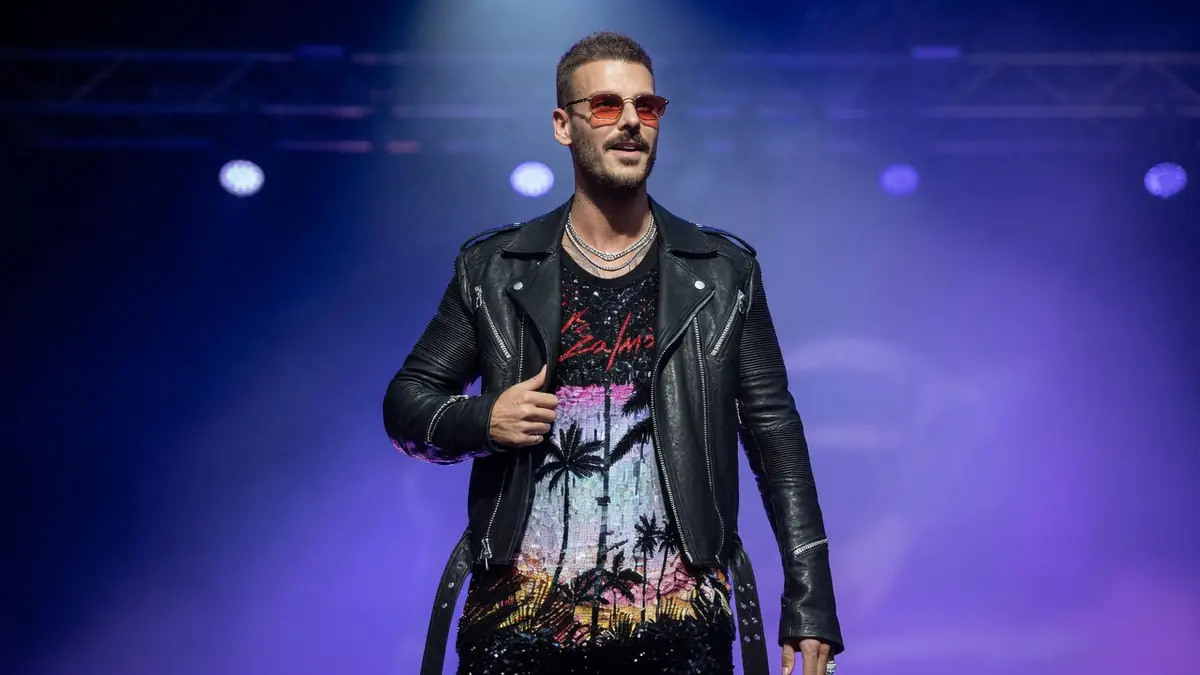 Matthieu Tota se tient sur scène en veste en cuir et lunettes de soleil sous lumières violettes