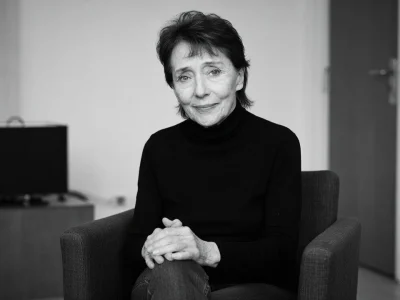 Mireille Perrier est assise dans un fauteuil les mains croisées.