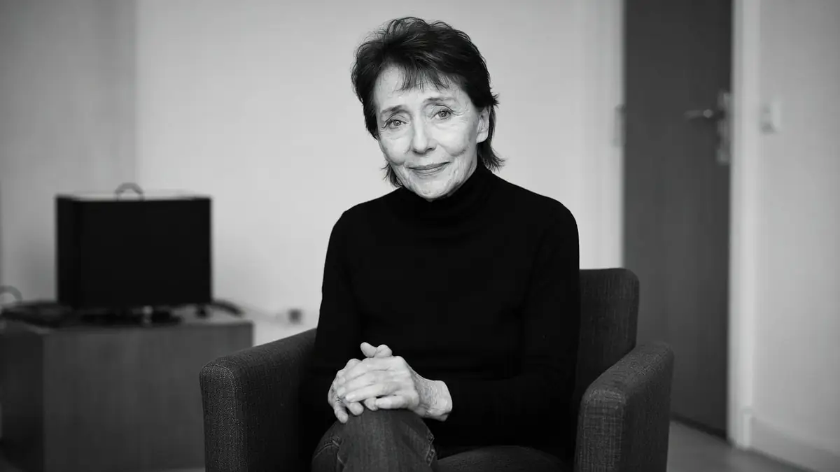 Mireille Perrier est assise dans un fauteuil les mains croisées.
