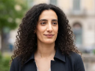 Portrait de Mouna Soualem avec ses longs cheveux bruns bouclés devant un arrière-plan urbain flou