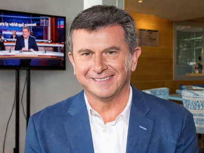 Pascal Bataille sourit devant un écran de télévision dans un espace intérieur moderne.