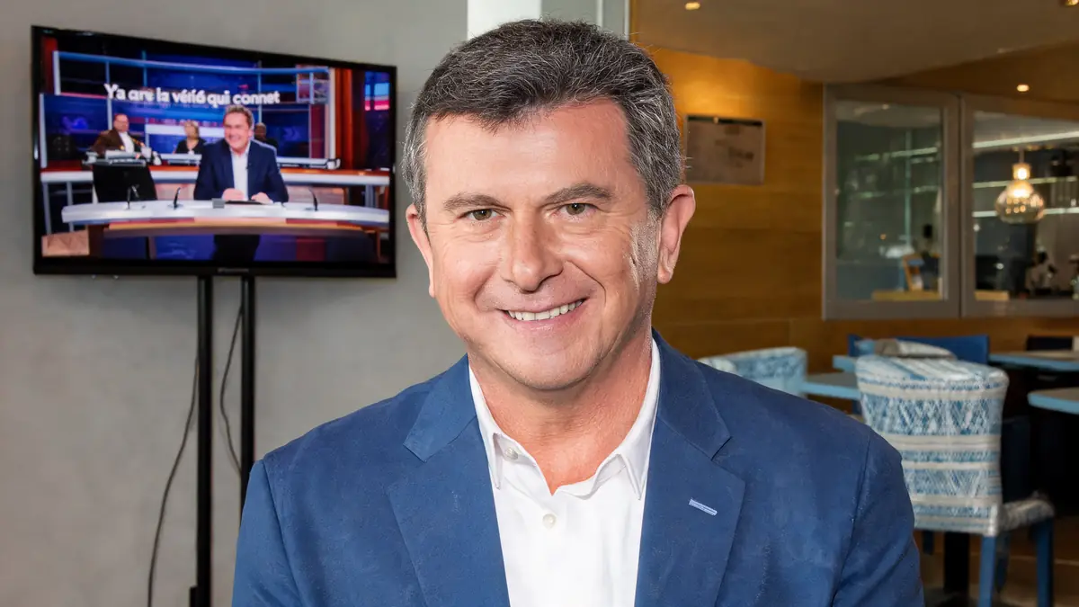Pascal Bataille sourit devant un écran de télévision dans un espace intérieur moderne.