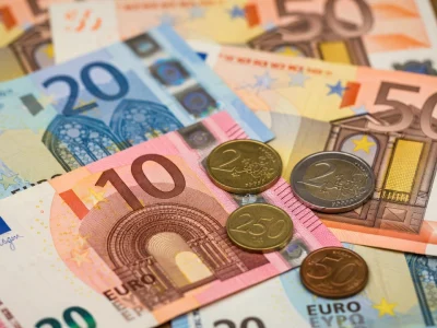 Des billets et pièces en euros étalés représentent l'argent liquide