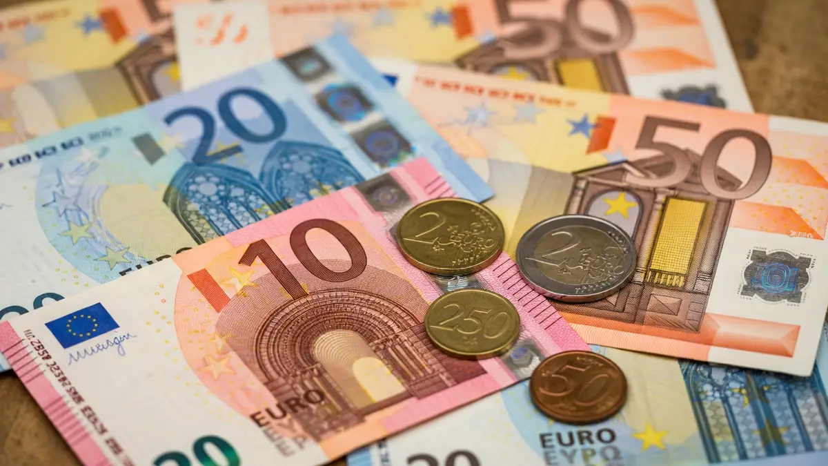 Des billets et pièces en euros étalés représentent l'argent liquide