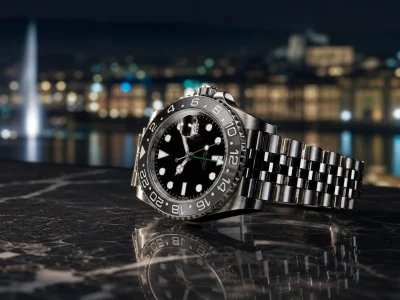Une Rolex Bruce Wayne posée sur une table sombre face aux lumières de Genève.
