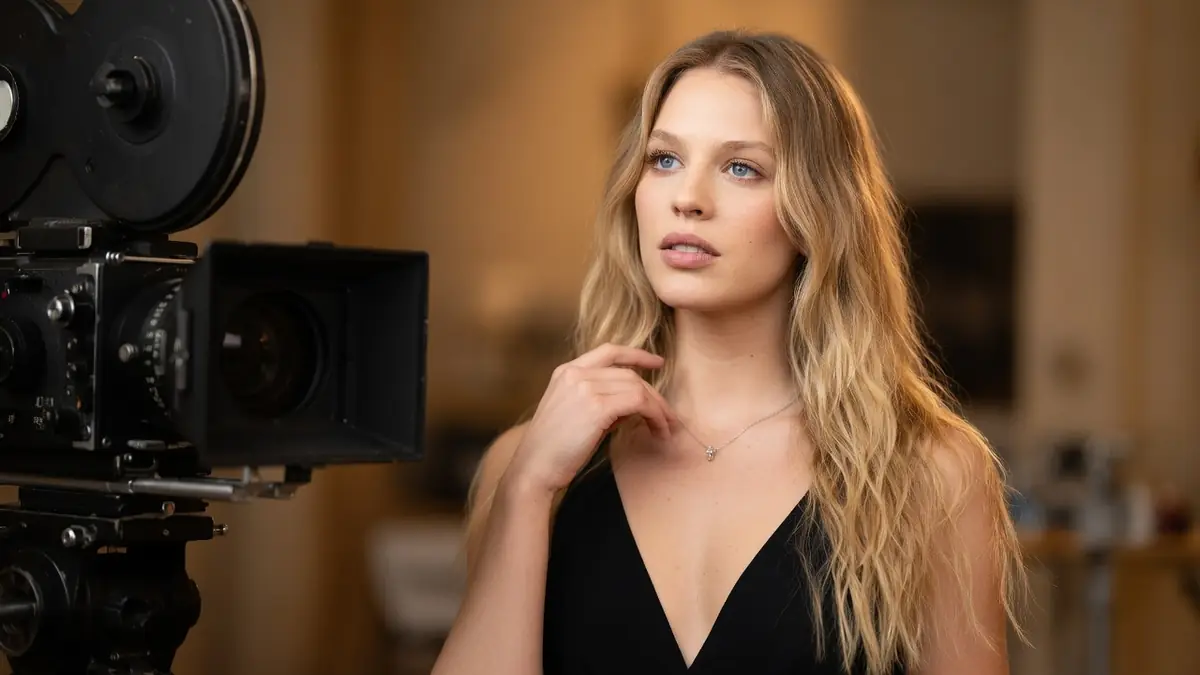Shanna Besson pose avec élégance devant une caméra de cinéma vintage dans un studio lumineux