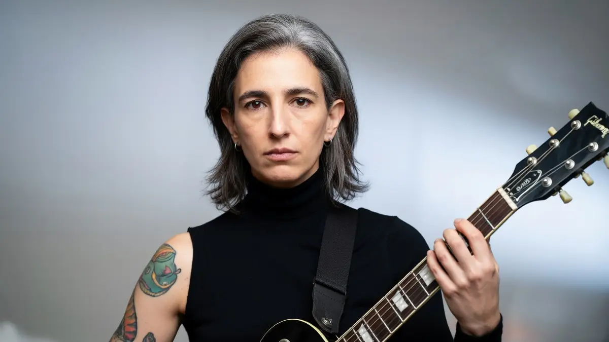 Portrait de Soraya Garlenq tenant une guitare électrique avec des tatouages visibles sur le bras