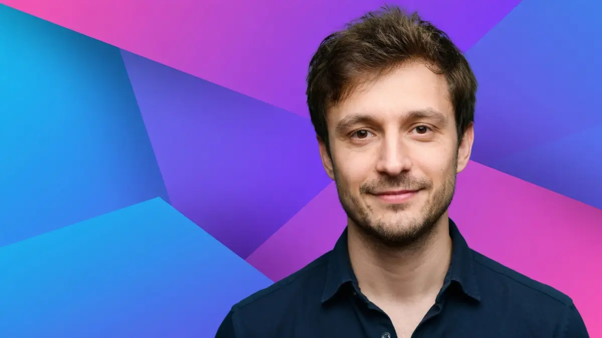 Tom Hudson pose devant un fond aux formes géométriques colorées