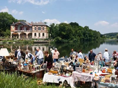 Une brocante dans le 57 rassemble de nombreux visiteurs au bord d'un lac devant une grande maison