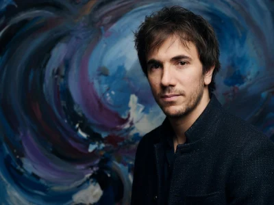 Xavier Guelfi pose devant un fond abstrait tourbillonnant aux tons bleus et violets