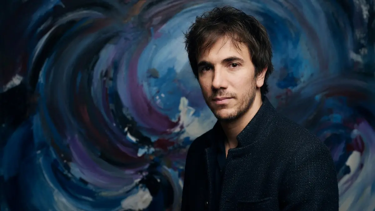 Xavier Guelfi pose devant un fond abstrait tourbillonnant aux tons bleus et violets
