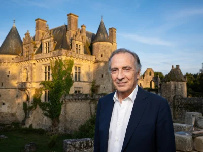 Yves Lecoq se tient devant un château de pierre baigné de lumière dorée