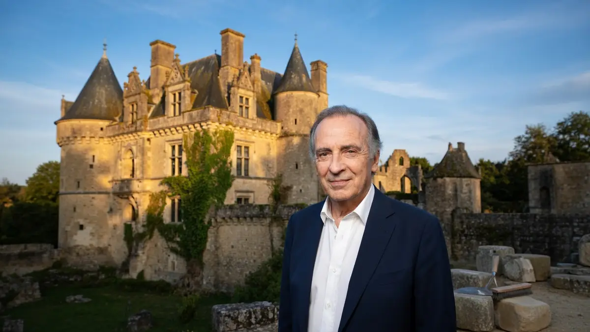 Yves Lecoq se tient devant un château de pierre baigné de lumière dorée
