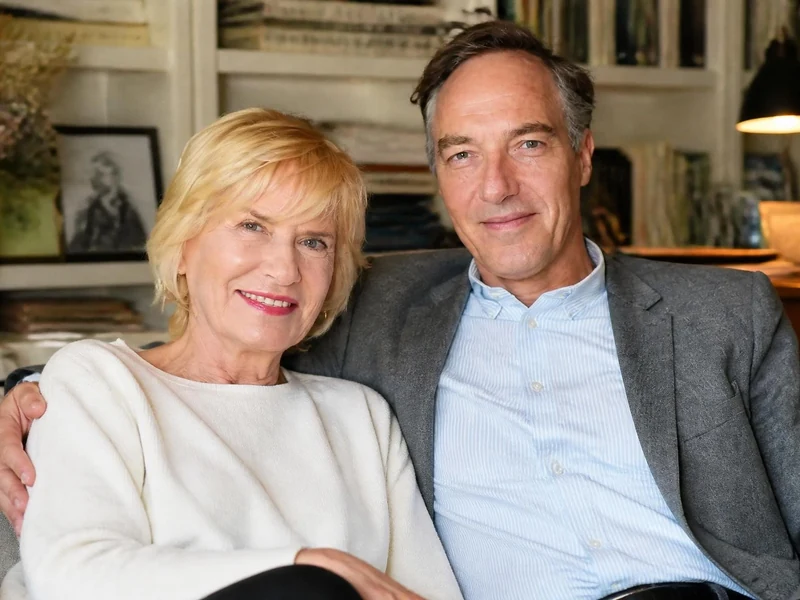 Catherine Ceylac son fils Jean-Philippe posent ensemble, souriants, assis sur un canapé dans un intérieur chaleureux