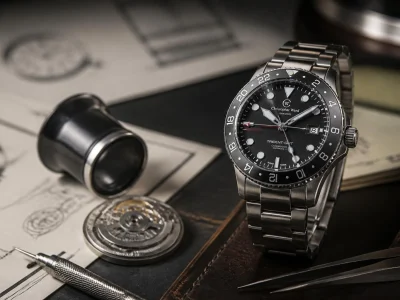 Une montre Christopher Ward élégante posée sur un plan de travail avec des outils d'horloger et des schémas techniques