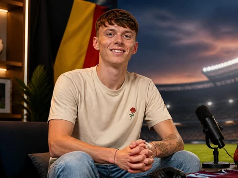 Ethan Hazard souriant assis dans un studio avec un ballon de football et un stade en arrière-plan
