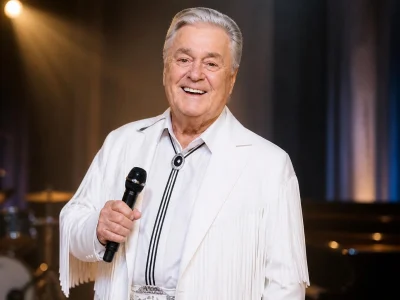 Gilles Girard sourit en tenant un micro et vêtu de son costume blanc emblématique sur scène