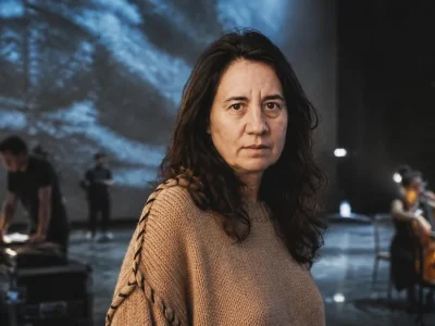Séverine Chavrier se tient au premier plan sur une scène de théâtre avec des musiciens en arrière-plan