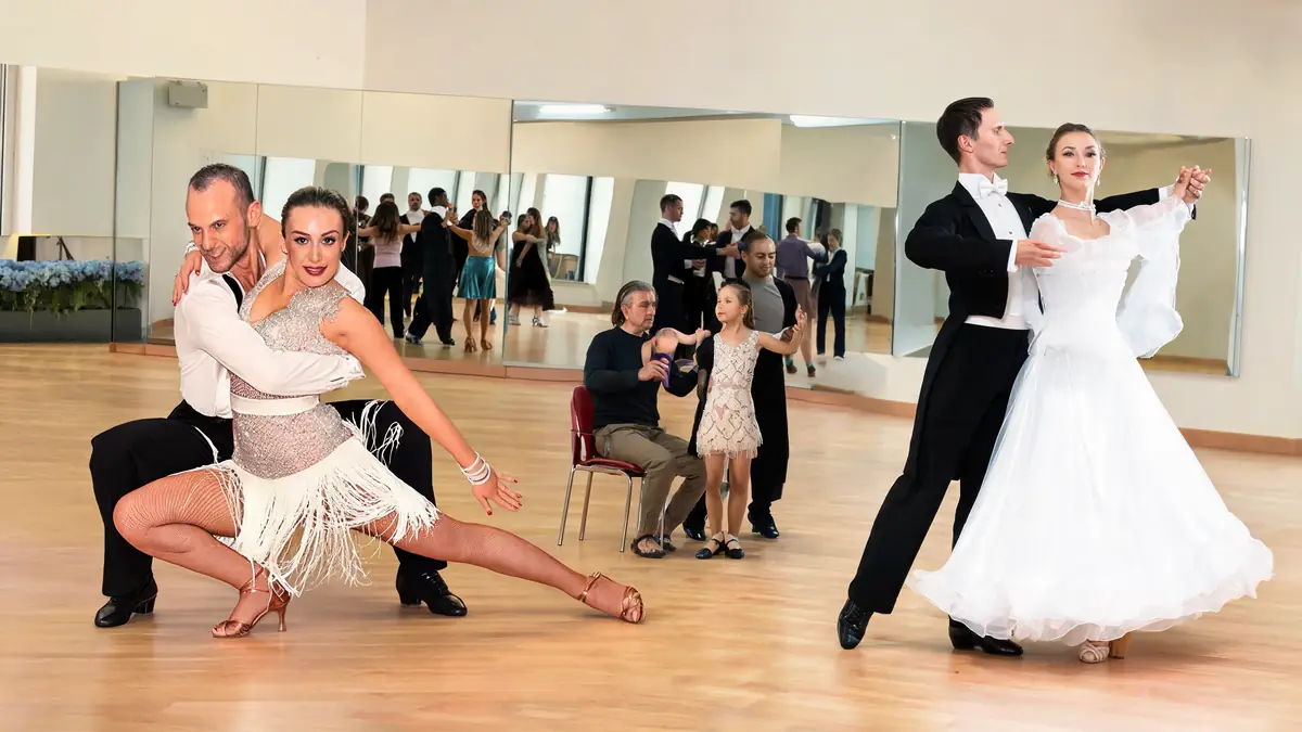 Des couples élégants pratiquent une danse de salon cours dans une salle de danse avec des miroirs