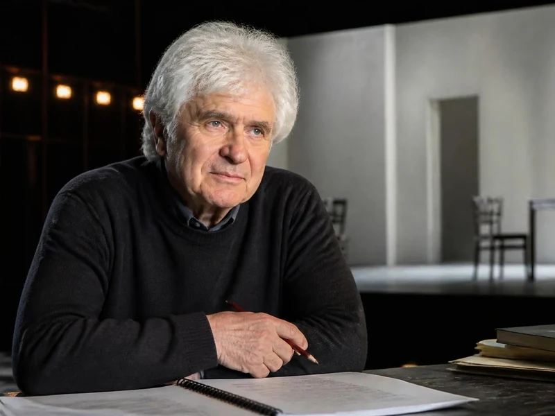 Portrait d Alain Françon assis à une table de travail avec des documents, sur le plateau d un théâtre