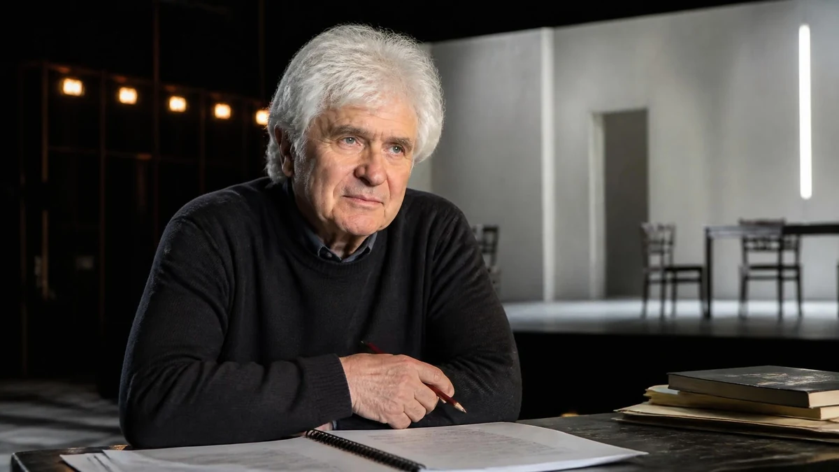 Portrait d Alain Françon assis à une table de travail avec des documents, sur le plateau d un théâtre