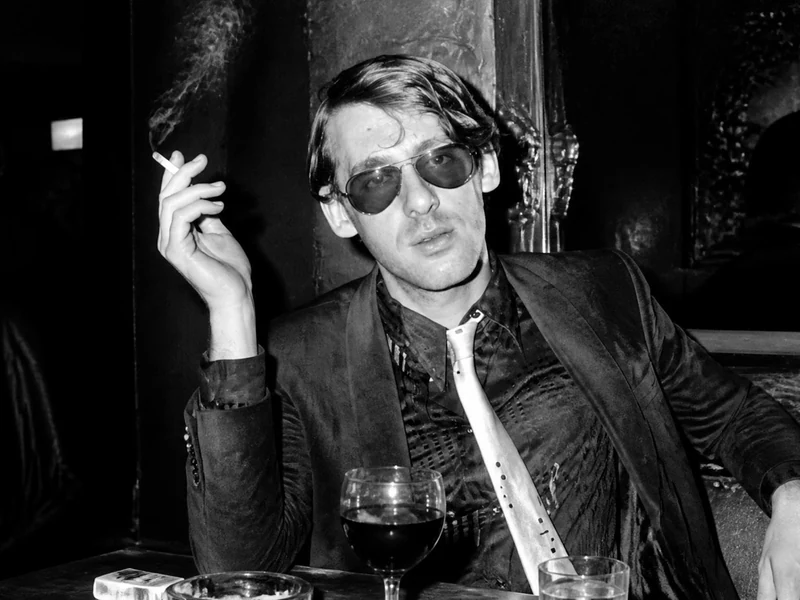 Portrait en noir et blanc d'Alain Pacadis fumant une cigarette dans un bar sombre