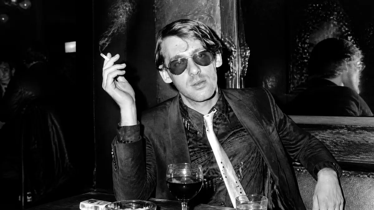 Portrait en noir et blanc d'Alain Pacadis fumant une cigarette dans un bar sombre