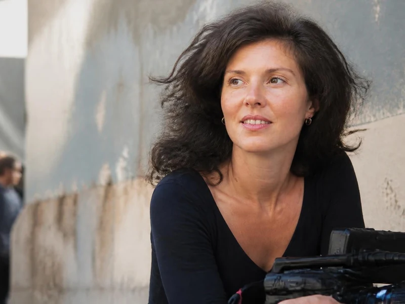 La réalisatrice Alexe Poukine souriante, tenant une caméra à l'épaule lors d'un tournage en extérieur