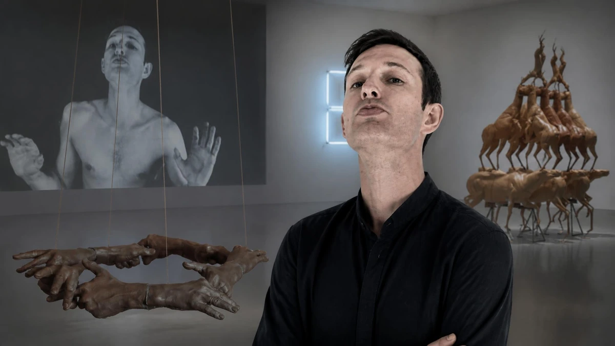 Un homme pose dans une galerie d'art contemporain entouré d'œuvres rappelant le style de Bruce Nauman