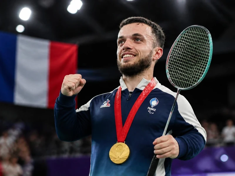 Charles Noakes célèbre sa victoire avec une médaille d'or autour du cou et une raquette de badminton à la main