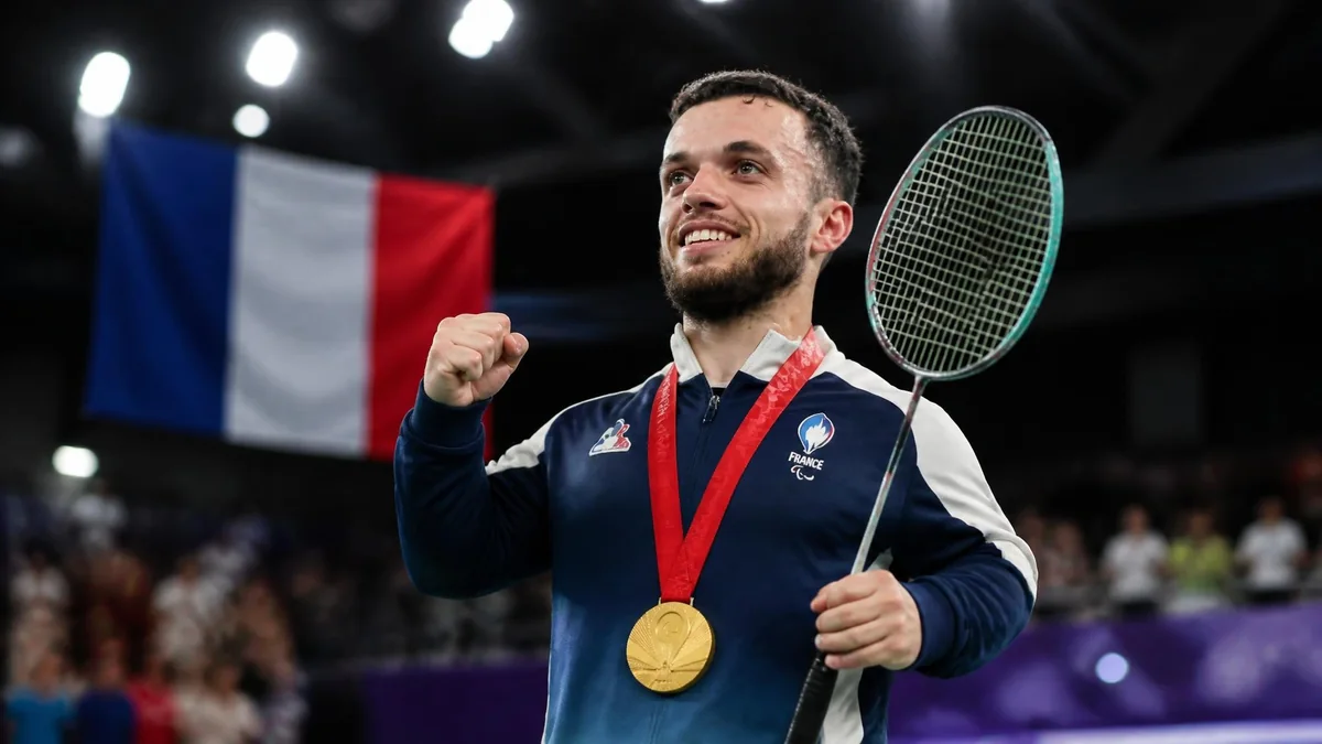 Charles Noakes célèbre sa victoire avec une médaille d'or autour du cou et une raquette de badminton à la main