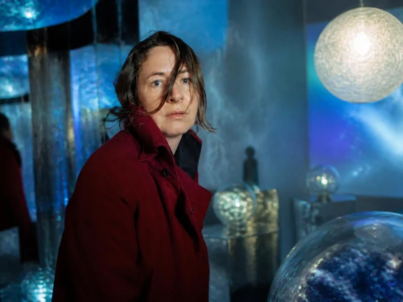 Dominique Gonzalez-Foerster porte un manteau rouge dans une installation artistique immersive aux lumières bleutées