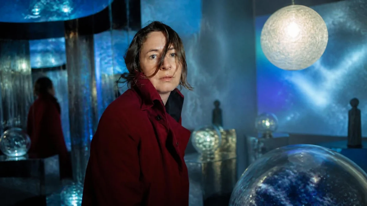 Dominique Gonzalez-Foerster porte un manteau rouge dans une installation artistique immersive aux lumières bleutées