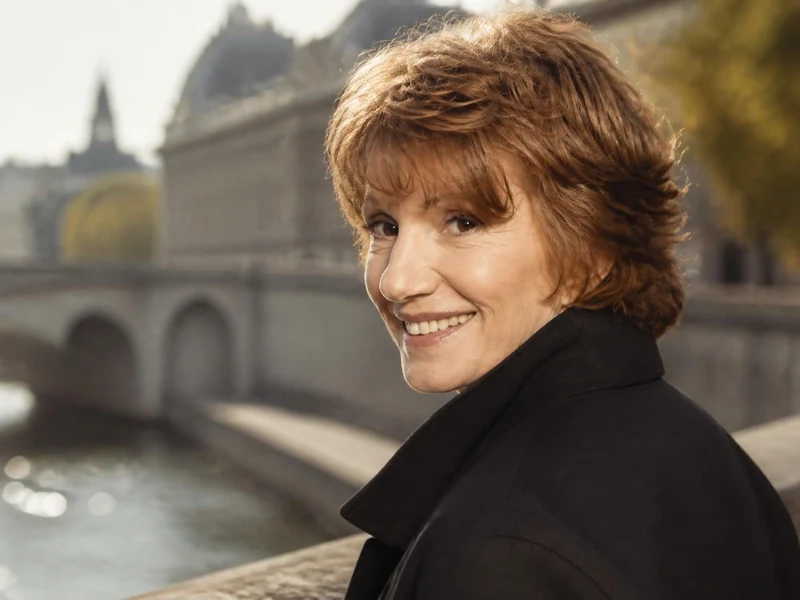 Portrait souriant de Dominique Labourier posant en extérieur avec un pont parisien en arrière-plan