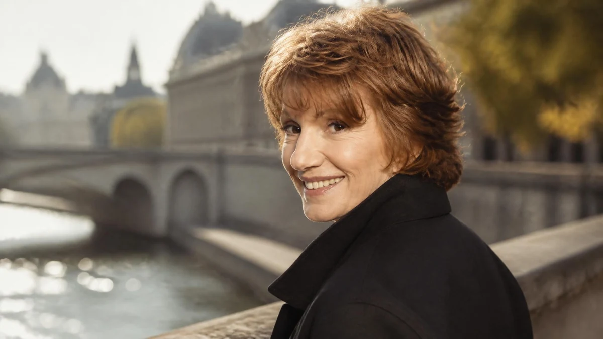 Portrait souriant de Dominique Labourier posant en extérieur avec un pont parisien en arrière-plan
