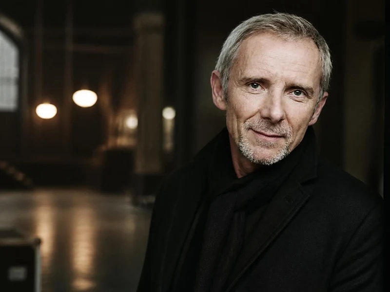 Portrait de l'acteur Geoffroy Thiébaut portant un manteau noir dans un décor intérieur sombre et élégant